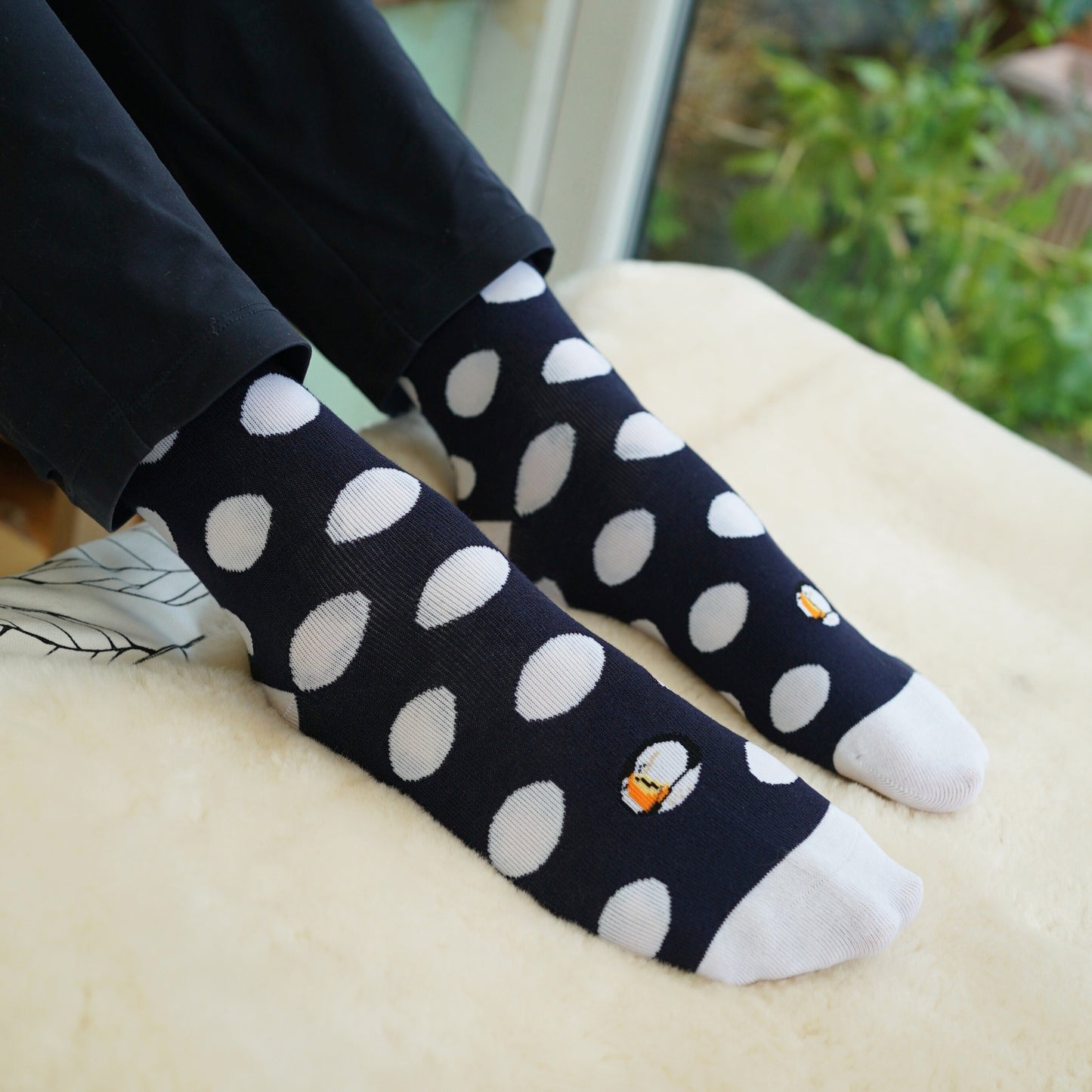 Black socks with white polka dots worn by a person sitting on a beige surface.