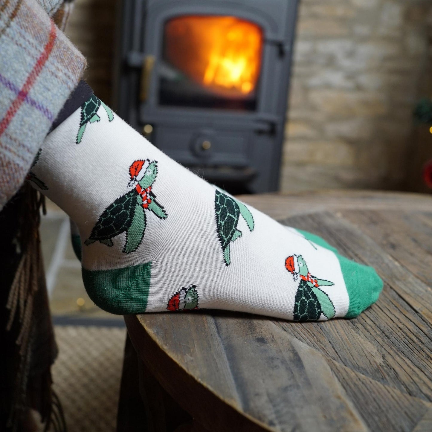 Sock with turtle design worn by a person in front of a lit fireplace.
