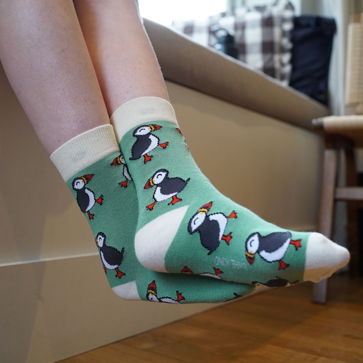 Green socks with puffin pattern worn by a person sitting on a couch.