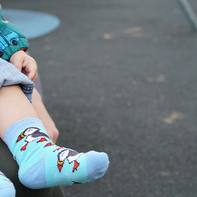 Child's foot wearing a blue sock with puffin design on a dark ground.