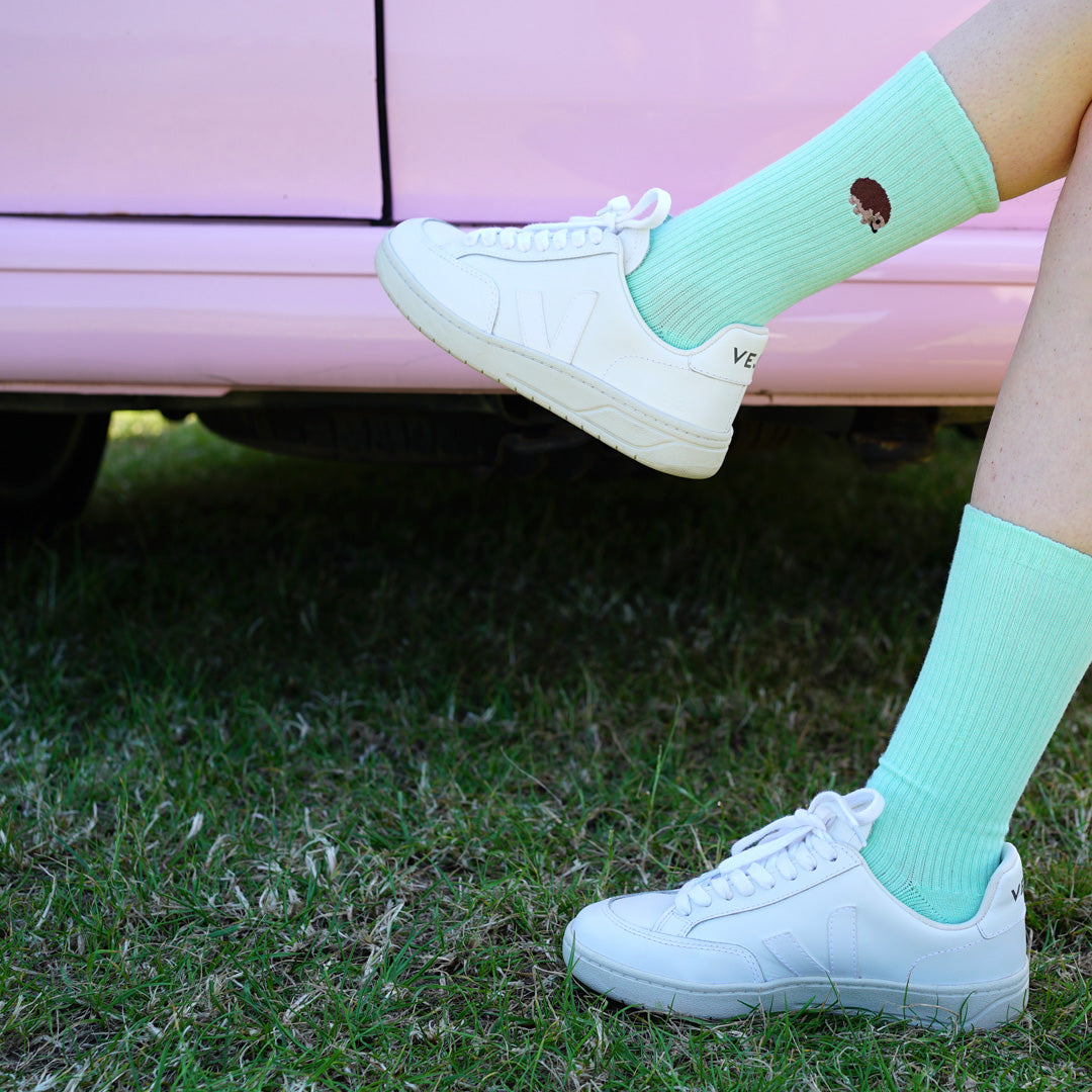 Model wearing green ribbed pastel socks with hedgehog motif embroidered on cuff 