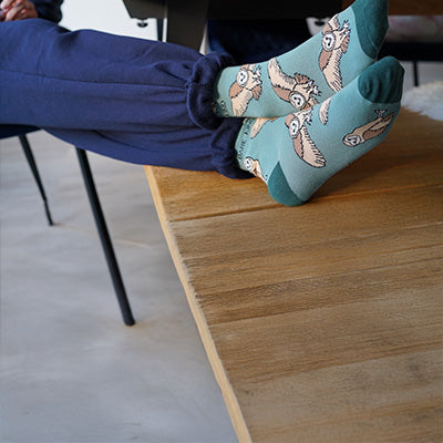 Barn owl socks worn by a person sitting on a wooden stool.