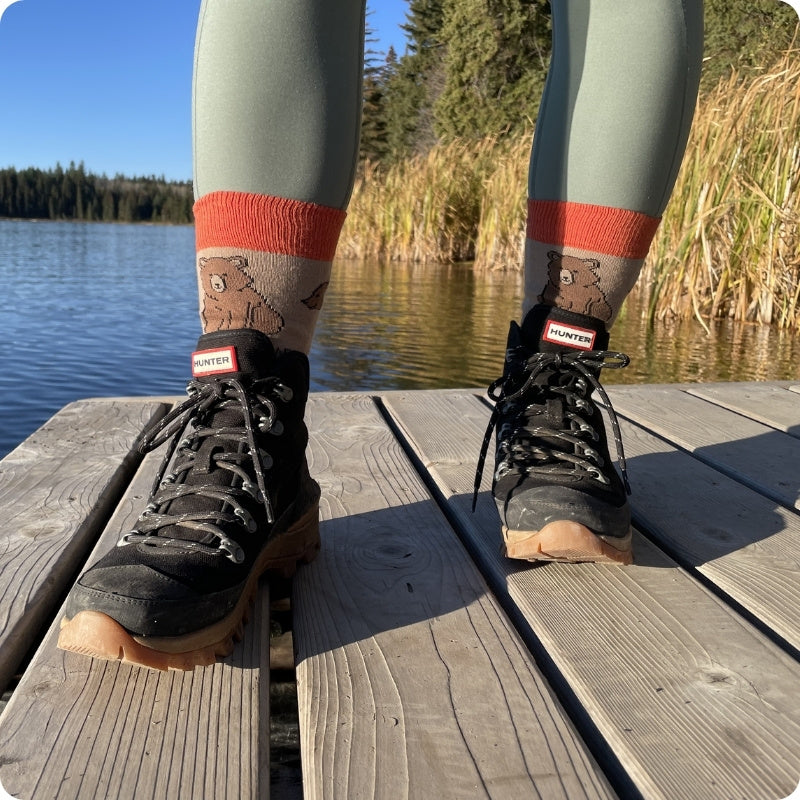 Person wearing hiking boots and patterned socks on a wooden dock by a lake.