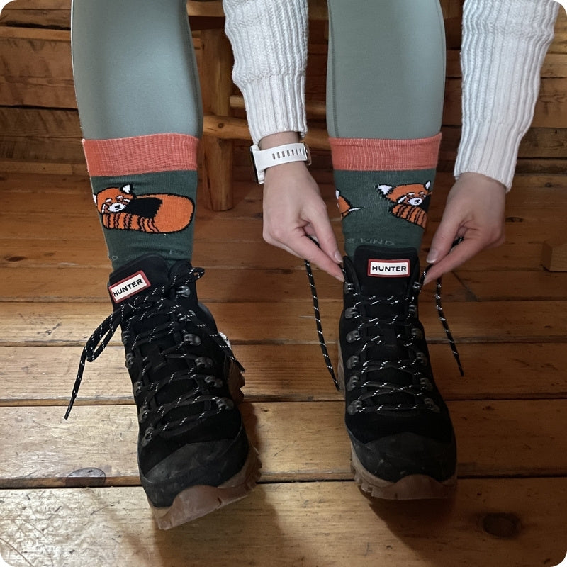 Person wearing green socks with red panda design and black Hunter boots on a wooden floor.