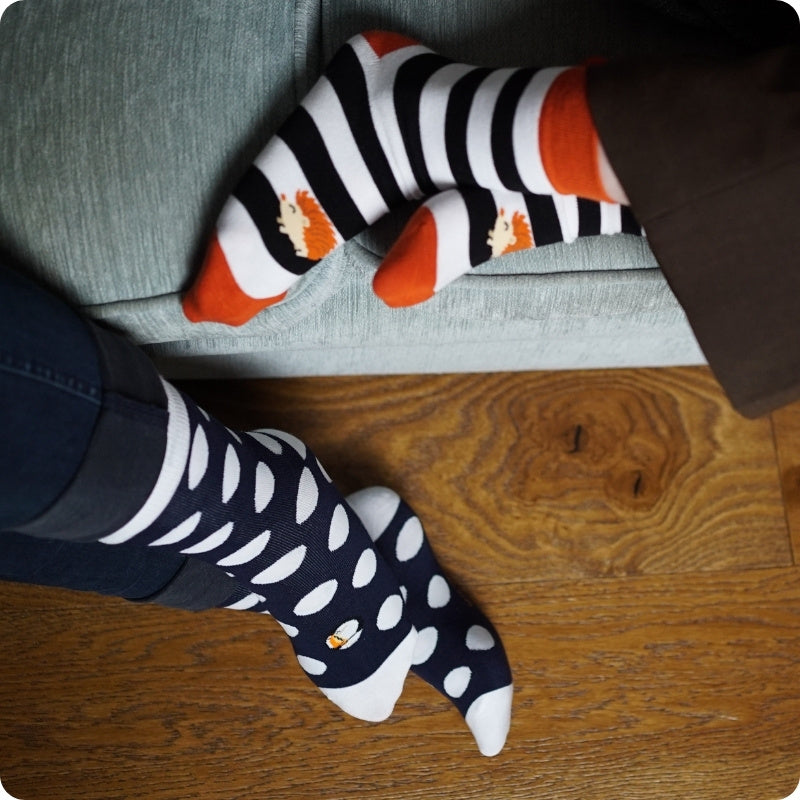 Person wearing black and white polka dot socks with orange and black striped socks on a wooden floor.