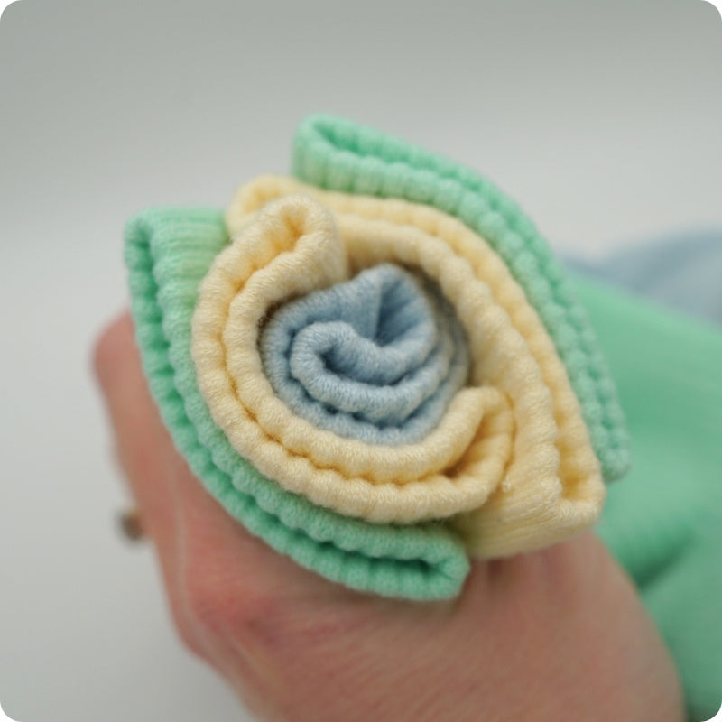 Rolled-up bamboo socks in green, yellow, and blue held by a hand on a light gray background