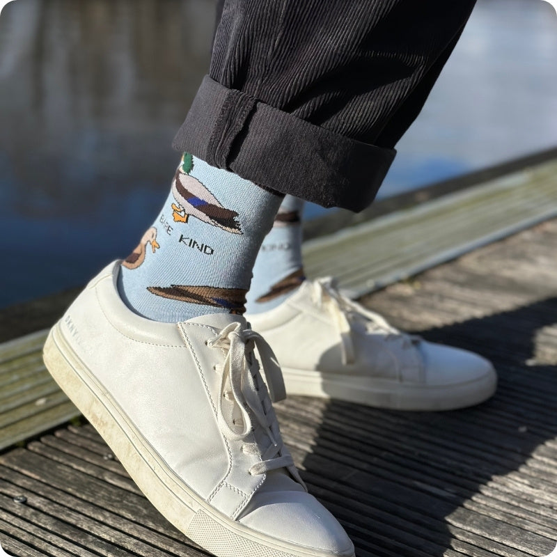 Person wearing light blue socks with animal designs and white sneakers on a wooden deck.