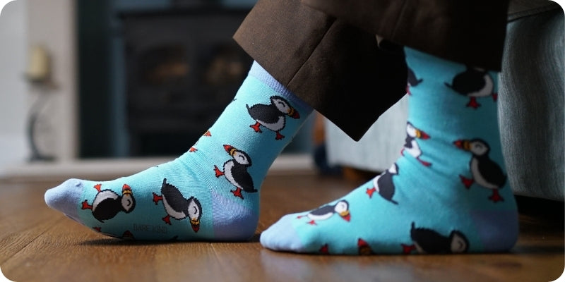 Blue socks with puffins design worn indoors on a wooden floor.
