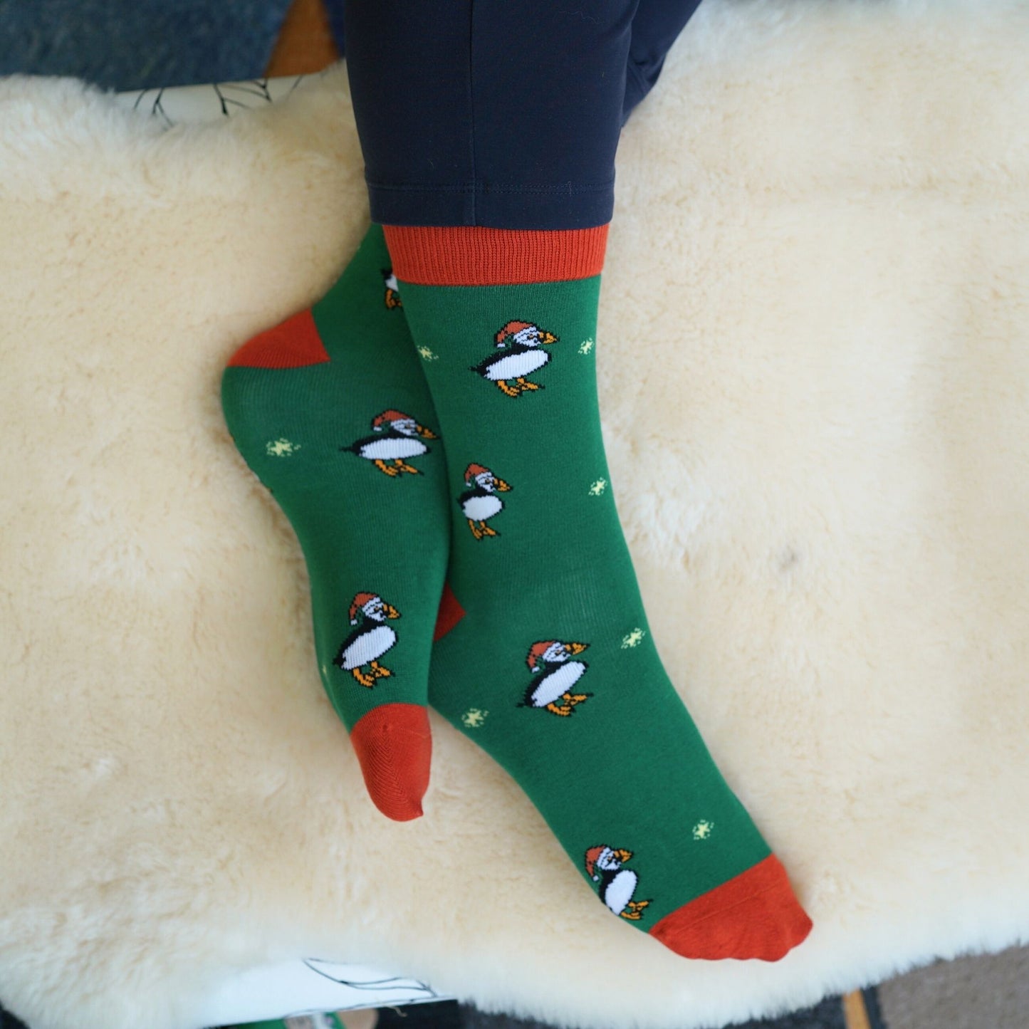 Green socks with puffin design and red accents worn on a white surface