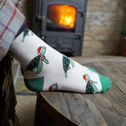 Sock with turtle design worn by a person in front of a lit fireplace.