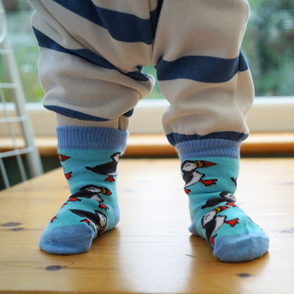 Children's legs wearing blue socks with puffin design on a wooden floor.