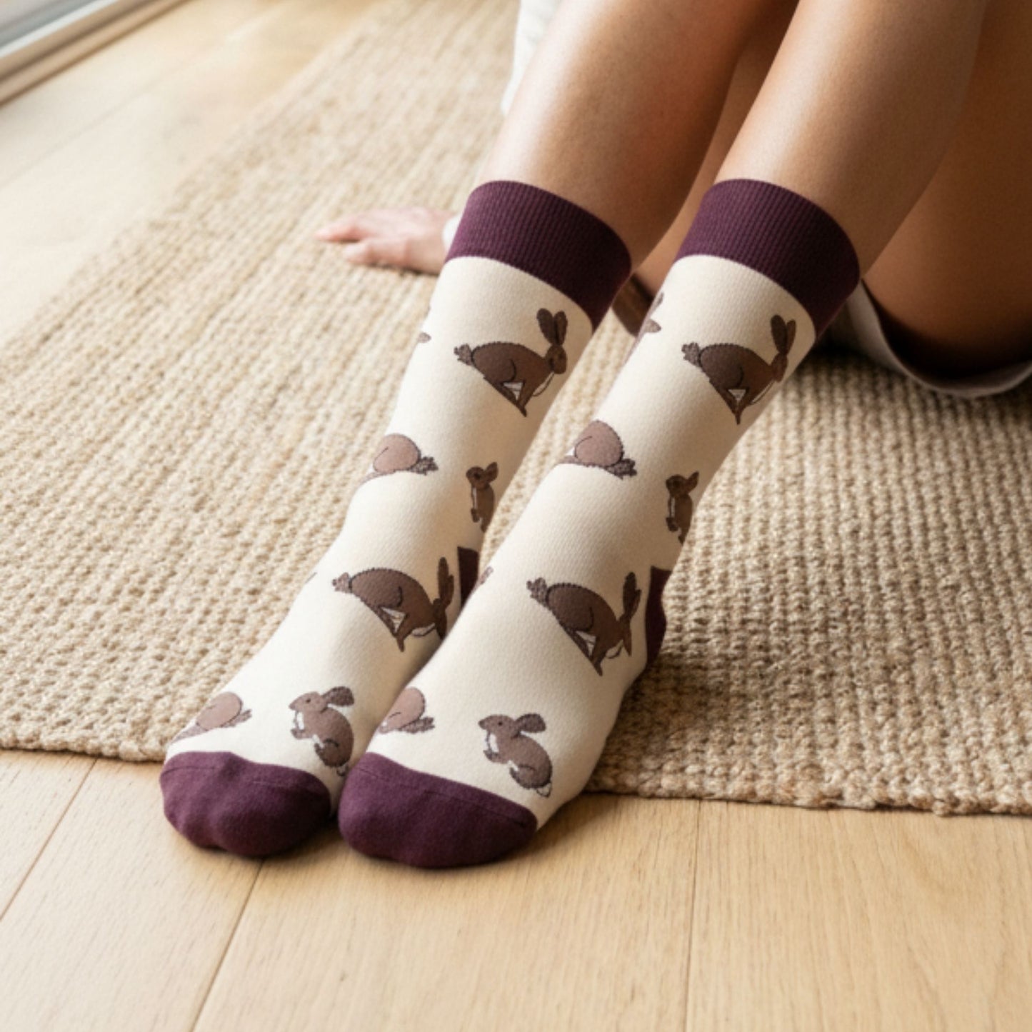 White socks with brown hare pattern and purple toes and cuffs worn by a person sitting on a wooden floor.
