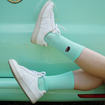 Model wearing a minimalist flat lay picture of pastel green ribbed socks with hedgehog motif design