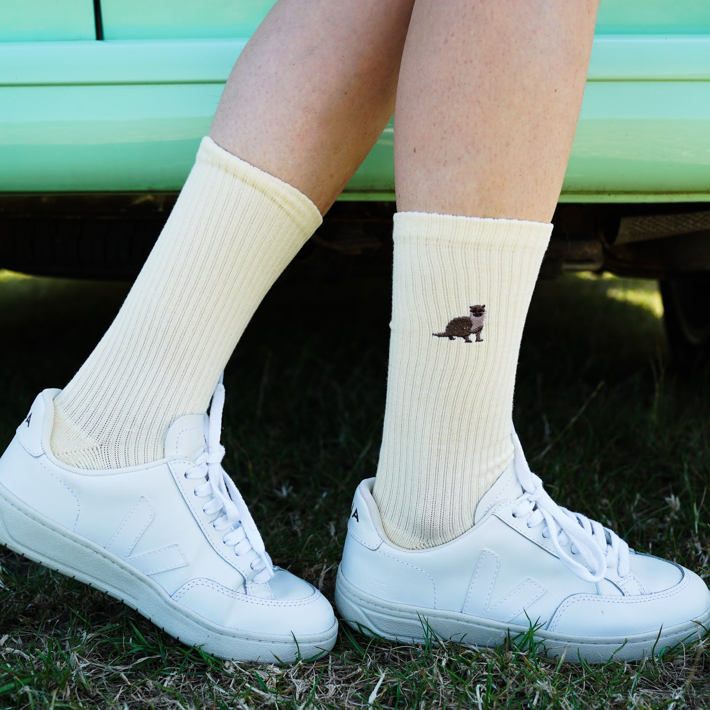 Model wearing pastel yellow ribbed bamboo socks with embroidered otter motif on the cuf