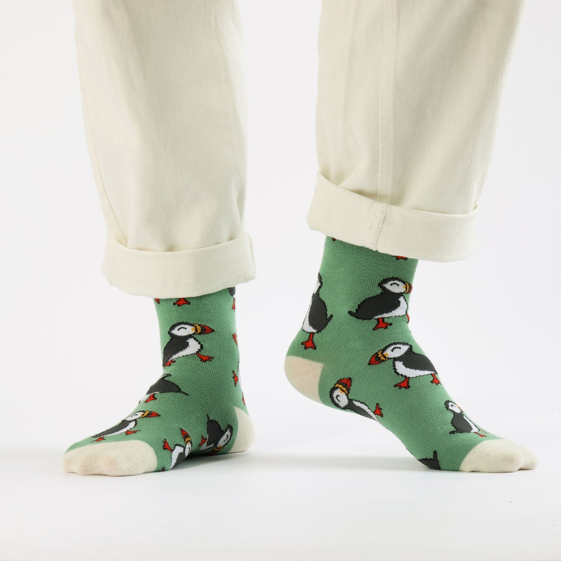 Green socks with puffin pattern worn by a person with beige pants on a white background