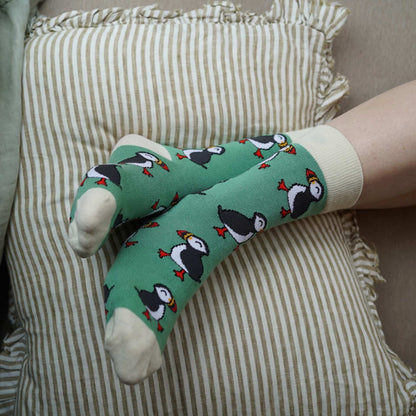 Person wearing green socks with puffin design on a striped cushion