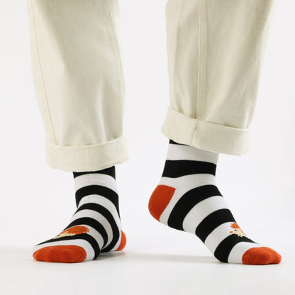 Black and white striped socks with orange toes and heels worn with beige pants on a white background