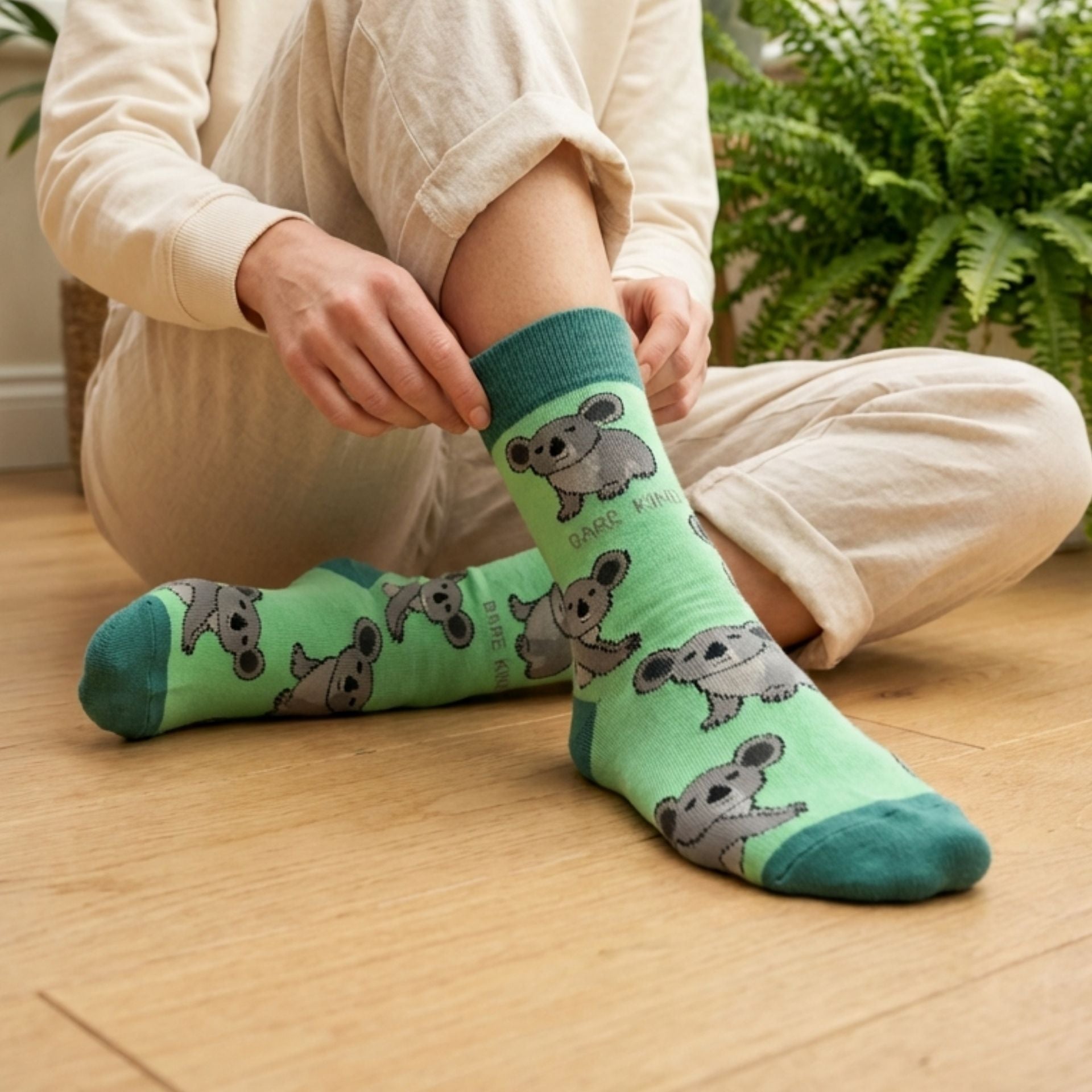 Person wearing green socks with koala designs on a wooden floor.