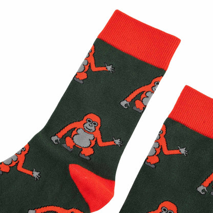 A pair of dark green crew socks with bright orange cuffs, heels, and toes, featuring a repeating pattern of orangutans in orange and gray.