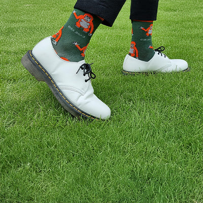 Person wearing green socks with orangutan designs and white shoes on grass