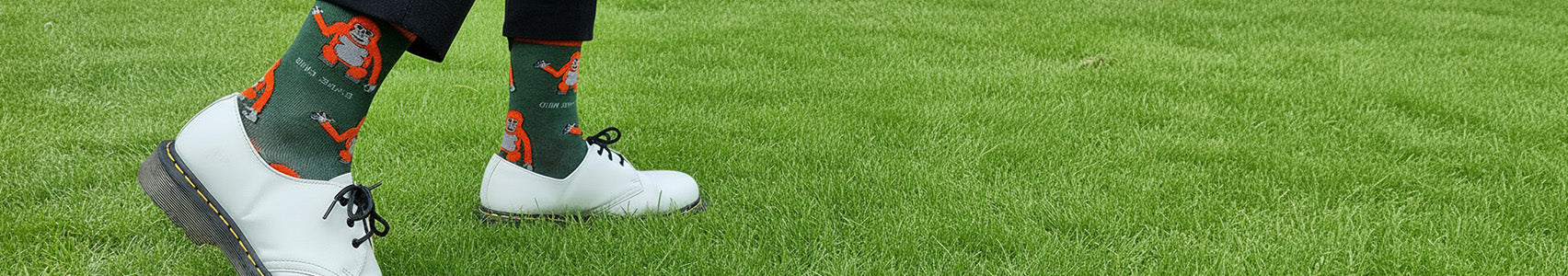 Person wearing green socks with orangutan designs and white shoes on grass