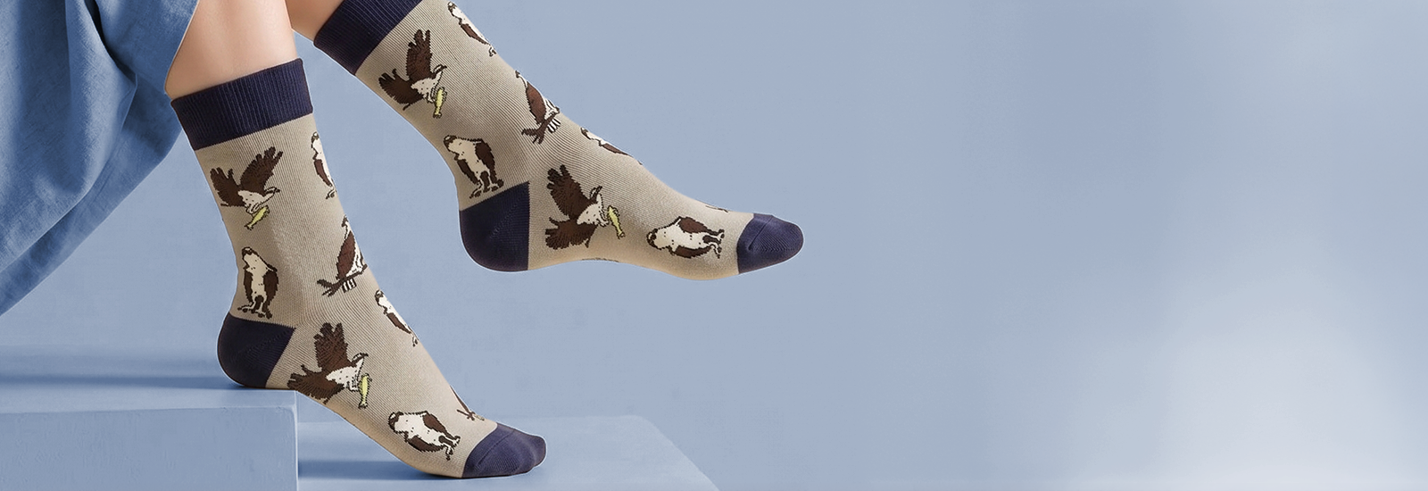 A pair of beige crew socks with a dark navy blue heel, toe, and cuff, featuring a pattern of flying ospreys. 