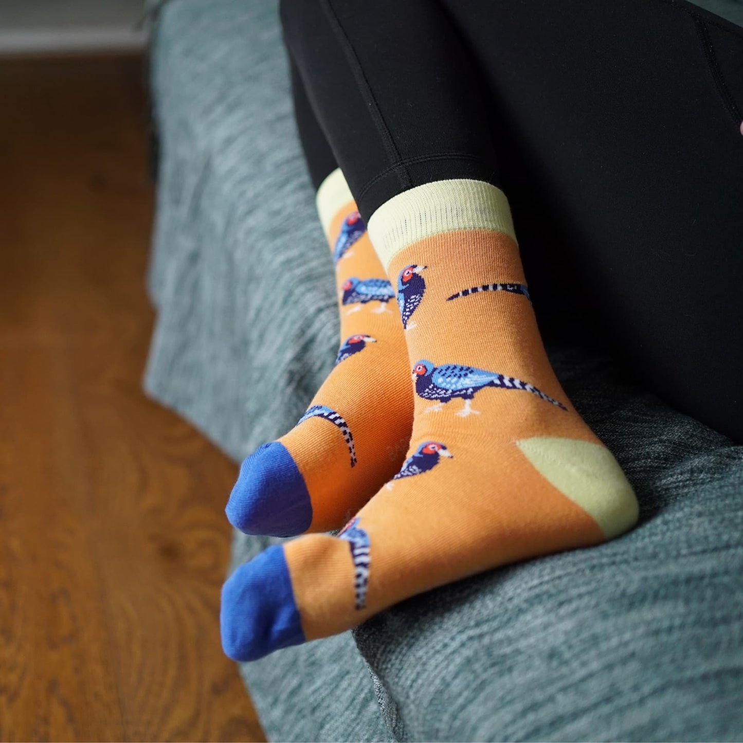 Person wearing orange socks with Pheasant design sitting on a couch.