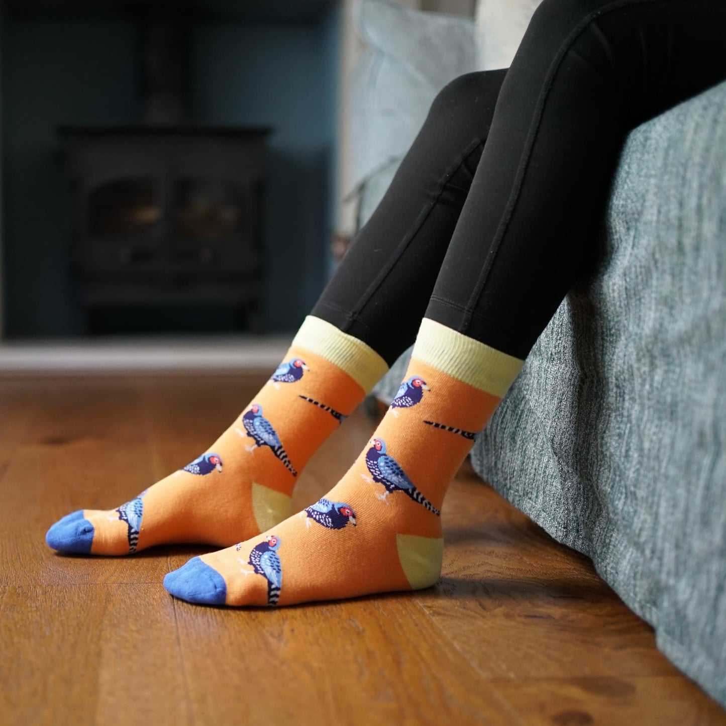 Person wearing orange socks with Pheasant design sitting on a couch.