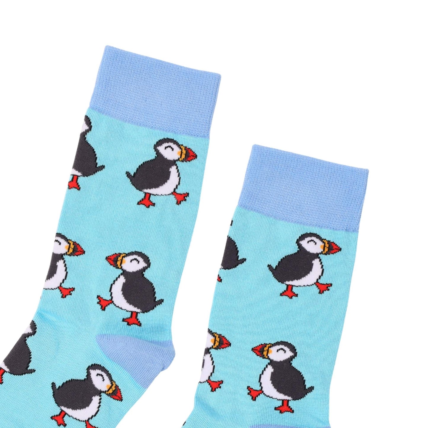 A pair of light blue crew socks with a repeating puffin pattern, featuring black and white bodies, red-orange beaks and feet, and light blue ribbed cuffs.