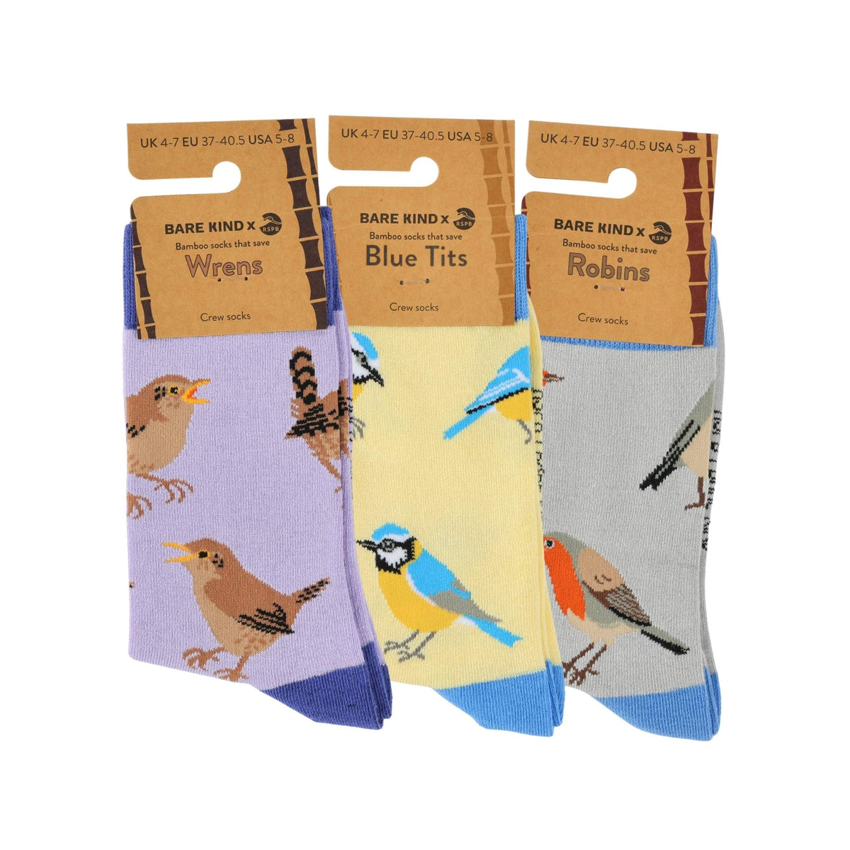 Three pairs of crew socks with bird illustrations, displayed side-by-side on their cardboard hanger packaging against a white background. The left pair is lavender with brown birds, the middle pair is pale yellow with blue birds, and the right pair is light gray with orange and brown birds.