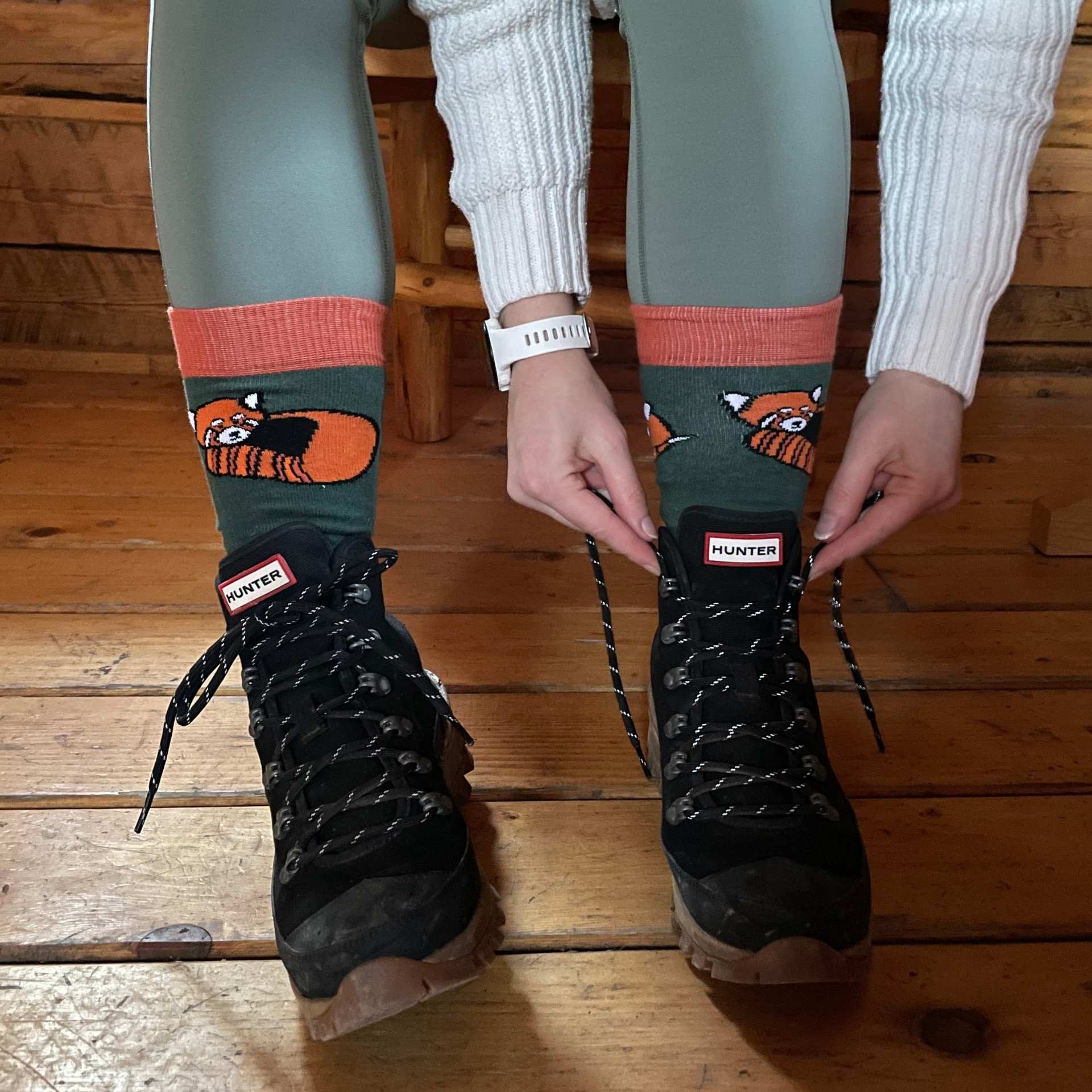 Person wearing green leggings and socks with red panda design, black Hunter boots on a wooden floor.