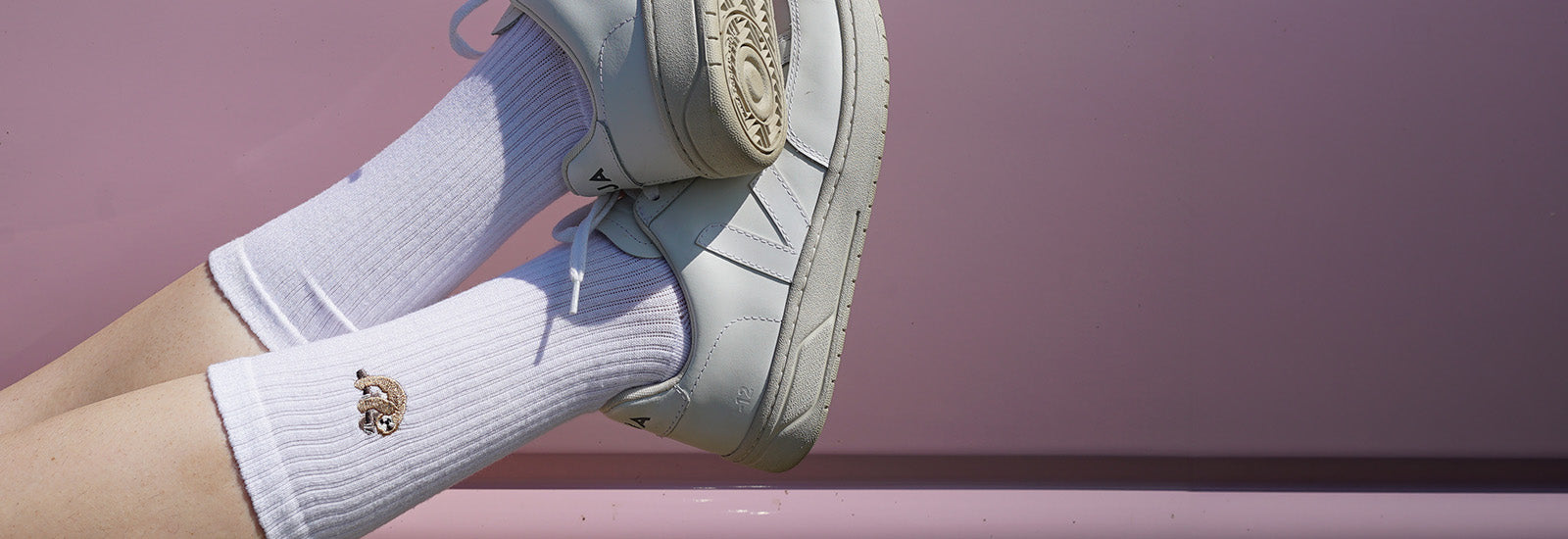 White socks with a sloth worn with light-colored sneakers on a pink background