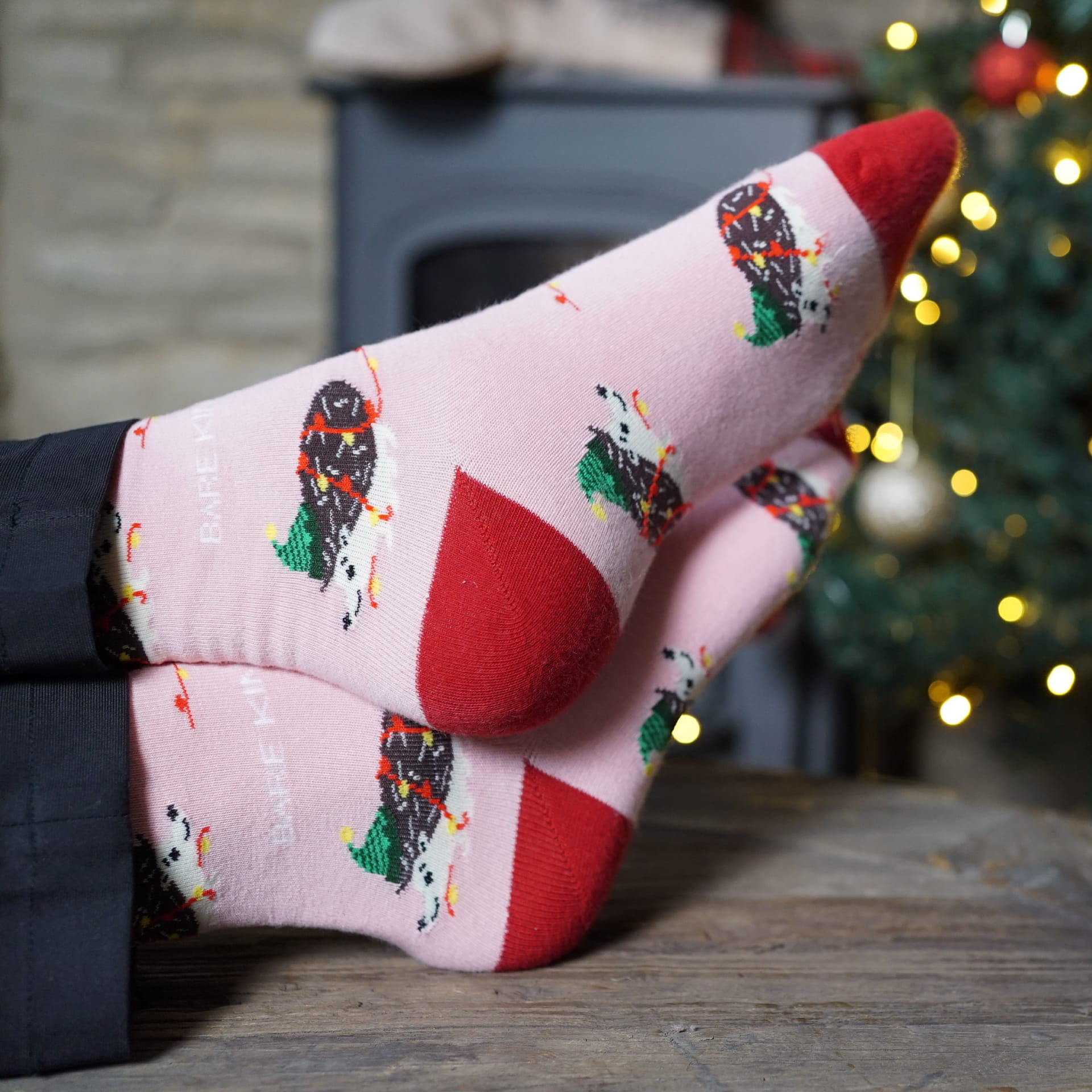 lifestyle image of model wearing pink christmas hedgehog bamboo socks in front of a christmas tree