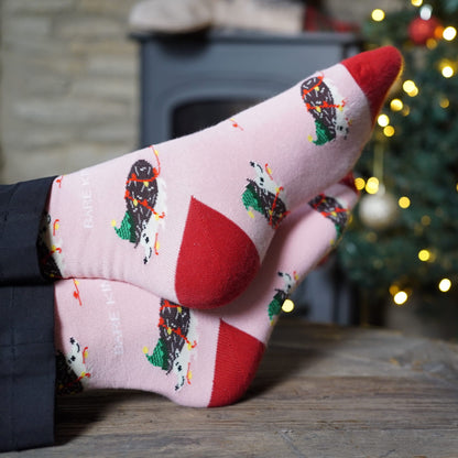 lifestyle image of model wearing pink christmas hedgehog bamboo socks in front of a christmas tree