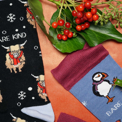 image of black christmas highland cow and blue christmas puffin bamboo socks with christmas foliage 