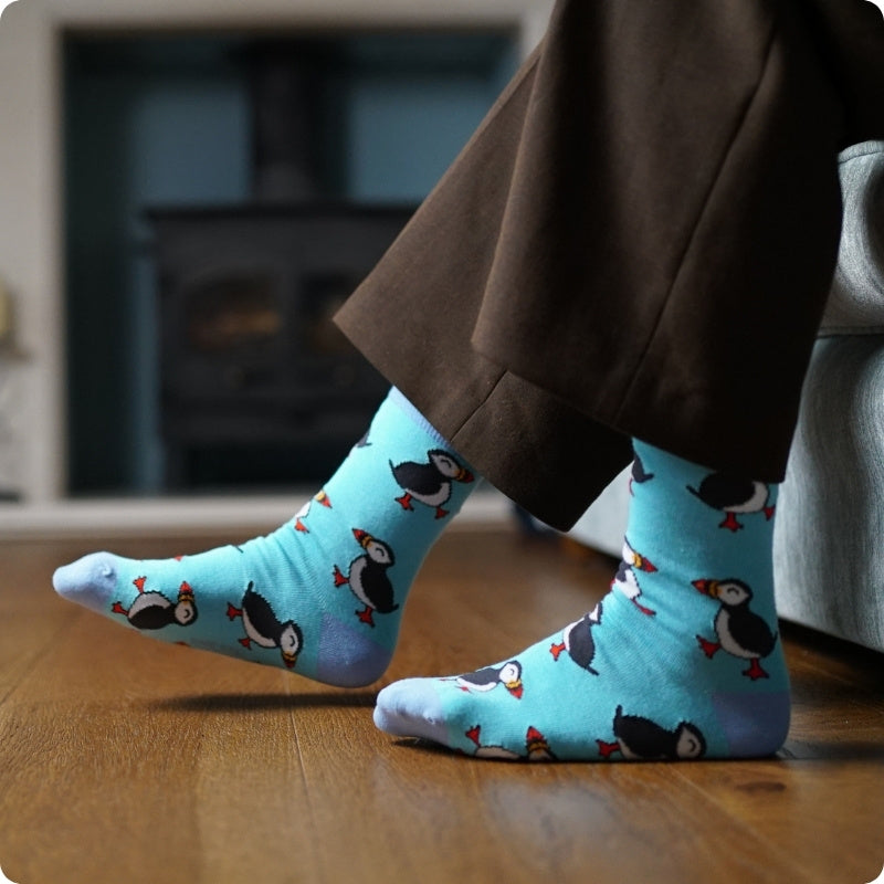 Person wearing blue puffin socks on a wooden floor.