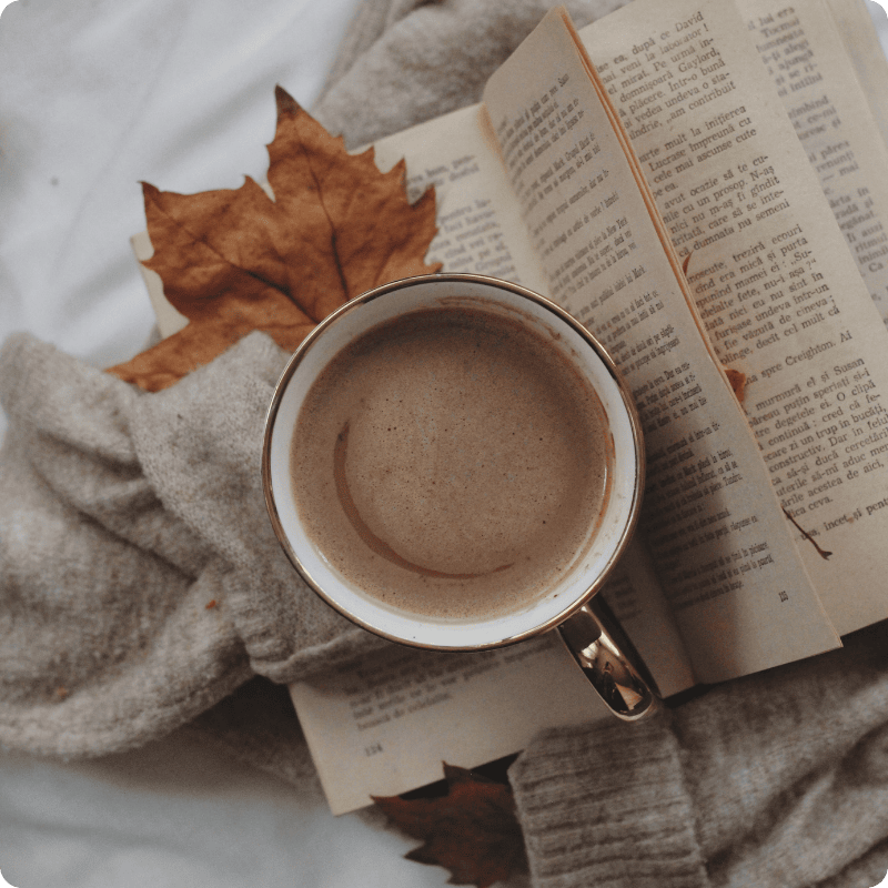 Cup of coffee with an open book and autumn leaves on a soft surface
