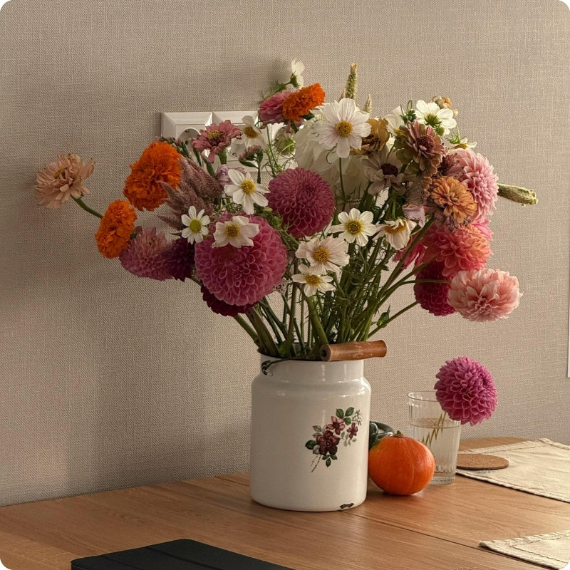 Bouquet of colorful flowers in a white vase on a wooden table with a neutral background