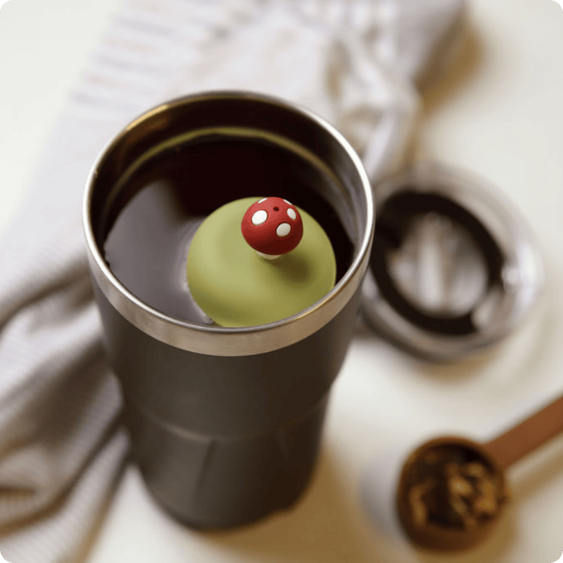 Green tea ball with a red mushroom on top in a black travel mug.