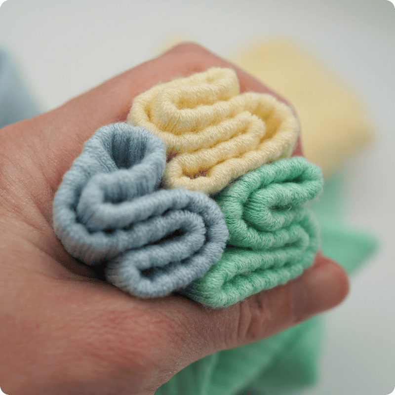 Three knitted yarn balls in blue, yellow, and green held in a hand.