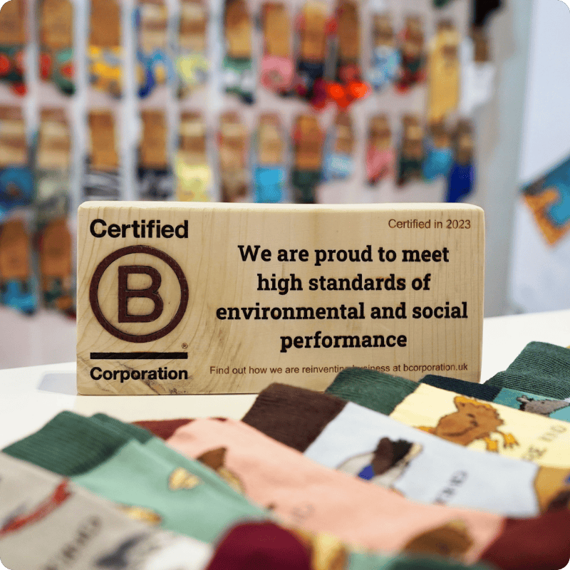 Wooden sign certifying B-Corporation status with colorful socks in the background