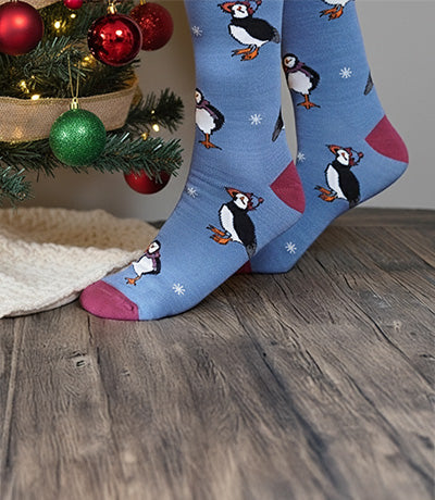 Blue socks with puffins design on a wooden floor next to a Christmas tree.