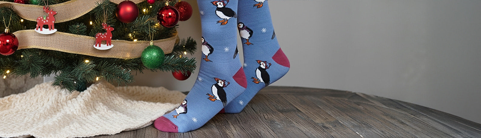 Blue socks with puffins design on a wooden floor next to a Christmas tree.