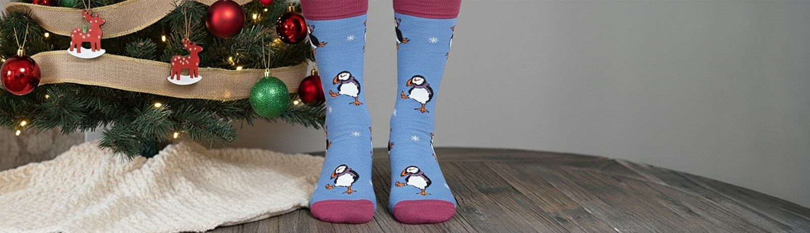 Person wearing blue socks with puffin design in front of a decorated Christmas tree.