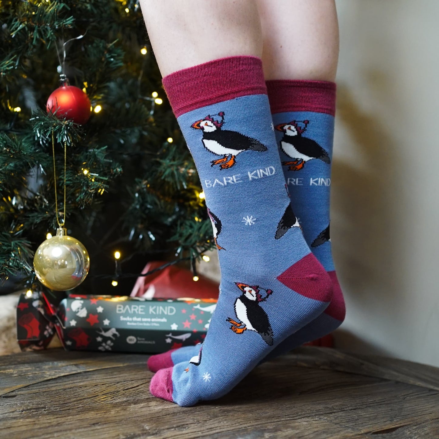 lifestyle image of model wearing blue christmas puffin bamboo socks by christmas tree