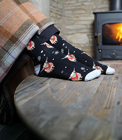 Person wearing socks with highland cows designs in front of a fireplace