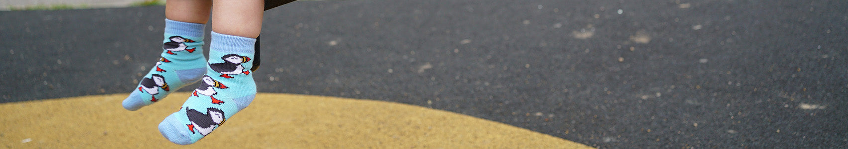 Kid wearing light blue puffin socks on a yellow and black surface