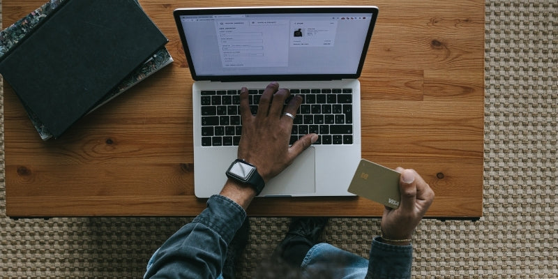 Person using a laptop with a credit card on a wooden desk