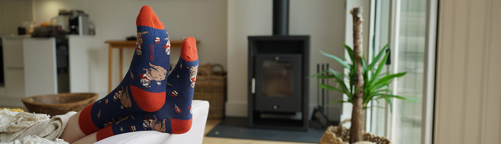 Person wearing blue christmas otter socks with red accents on a white couch in a living room.