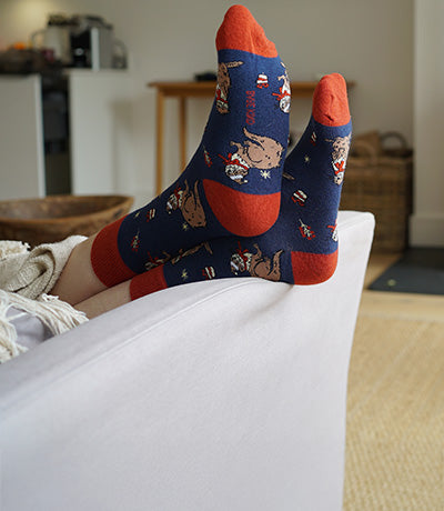 Person wearing blue christmas otter socks with red accents on a white couch in a living room.